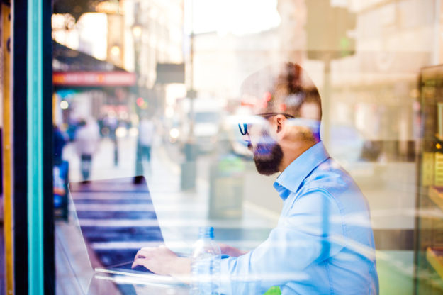 Hipster manager in cafe, working on laptop by window