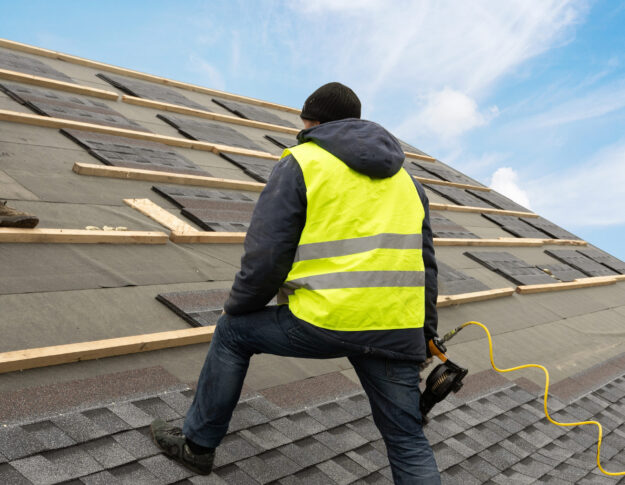 Workman using pneumatic nail gun install tile on roof of new house under construction