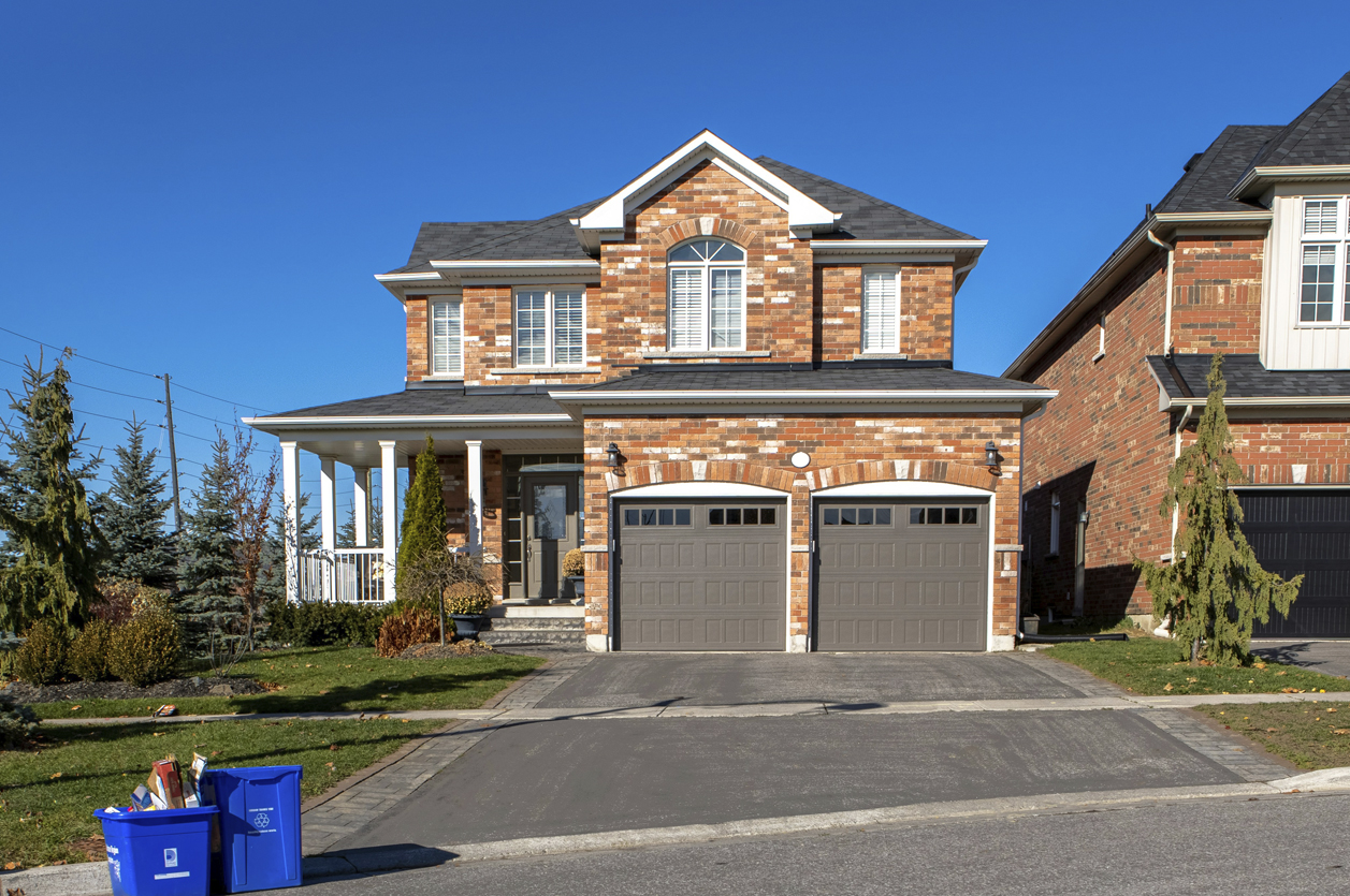 Beautiful Brick Home Exterior of large two-story brick home with two-car garage. Large blue recycling bins at the roadside and deep blue skies all around.