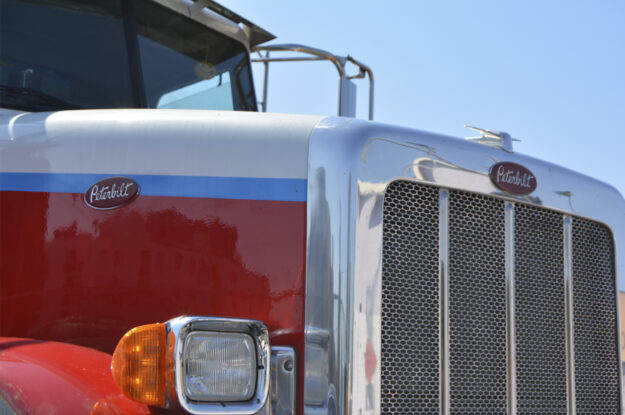 The imposing hood and grill at the front of a large Mack truck tractor.