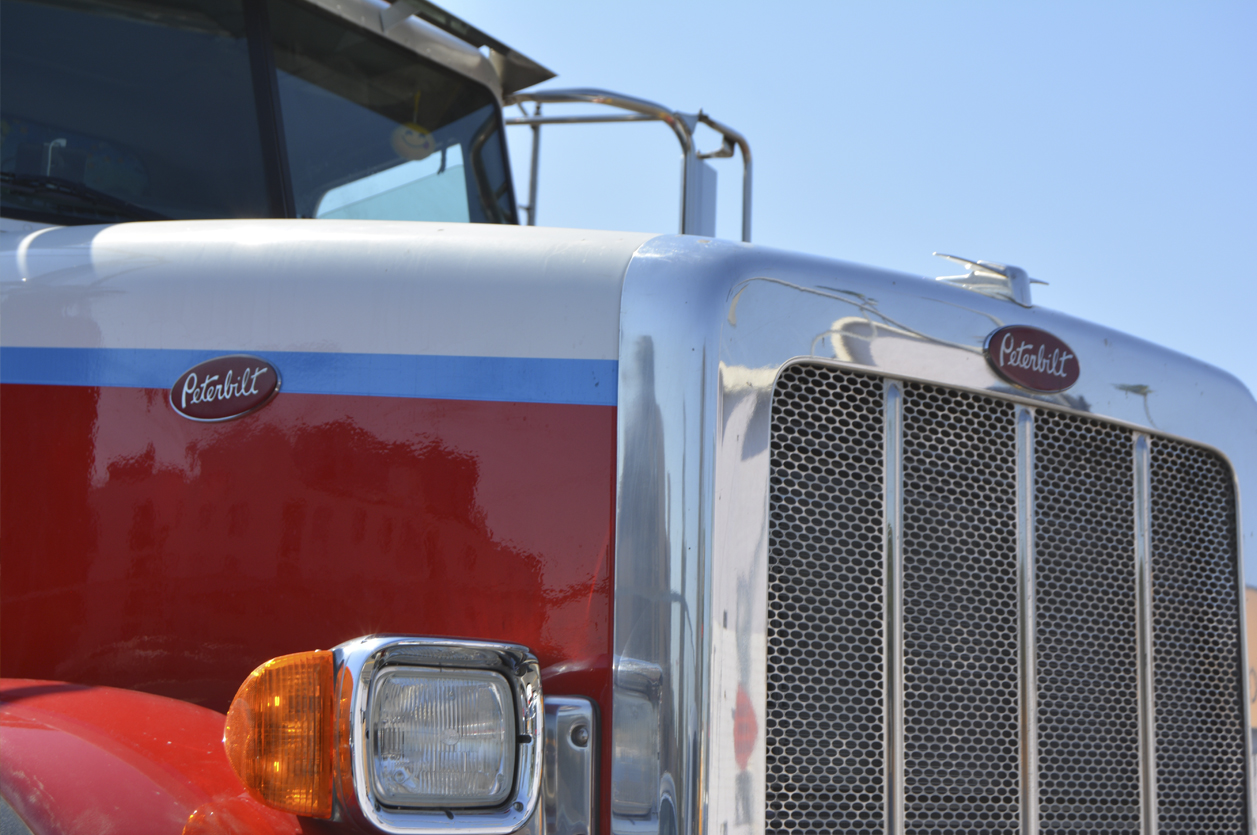 The imposing hood and grill at the front of a large Mack truck tractor.