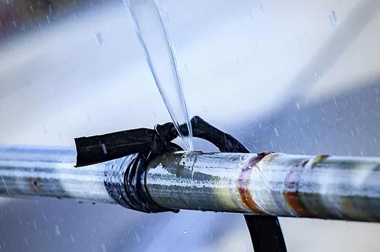 Close up photo of burst metal water pipe, forcefully shooting a stream of water up into the air.