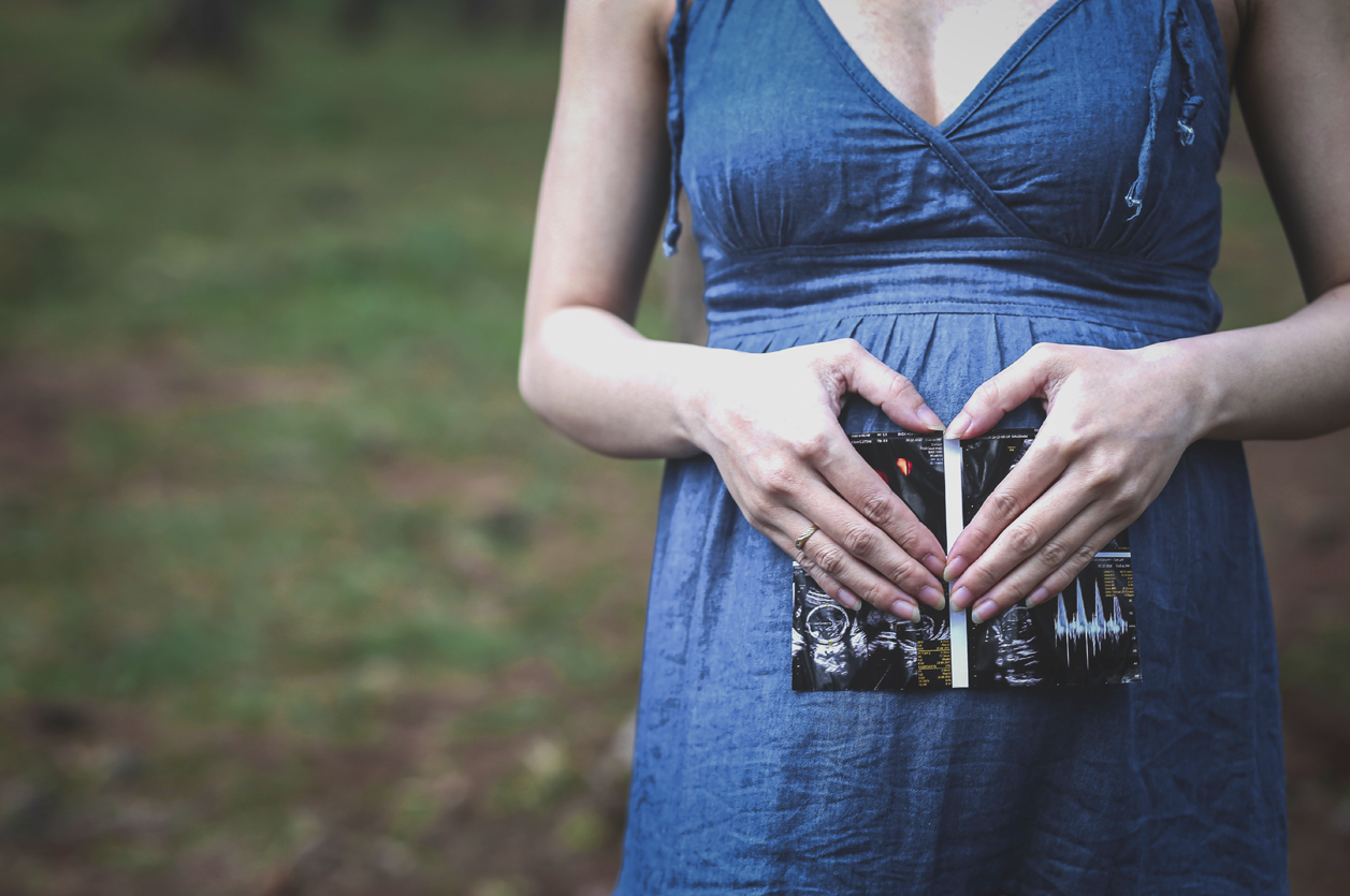 Pregnant Woman Pregnant woman in blue dress stands in a field, holding ultrasound photos of her unborn child.
