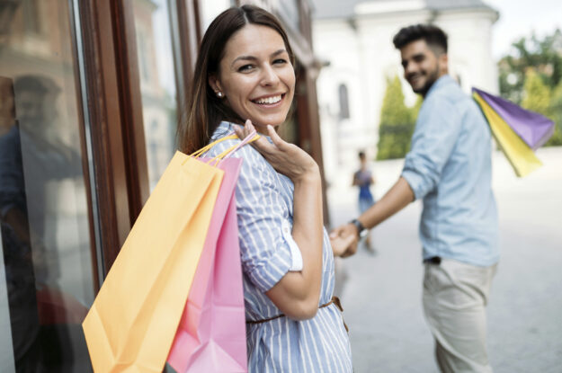 Portrait of smiling woman and her partner carrying shopping bags slung over their shoulders.