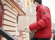 Man in winter coat carrying large boxes up a flight of stairs on the street to the entrance of a building.