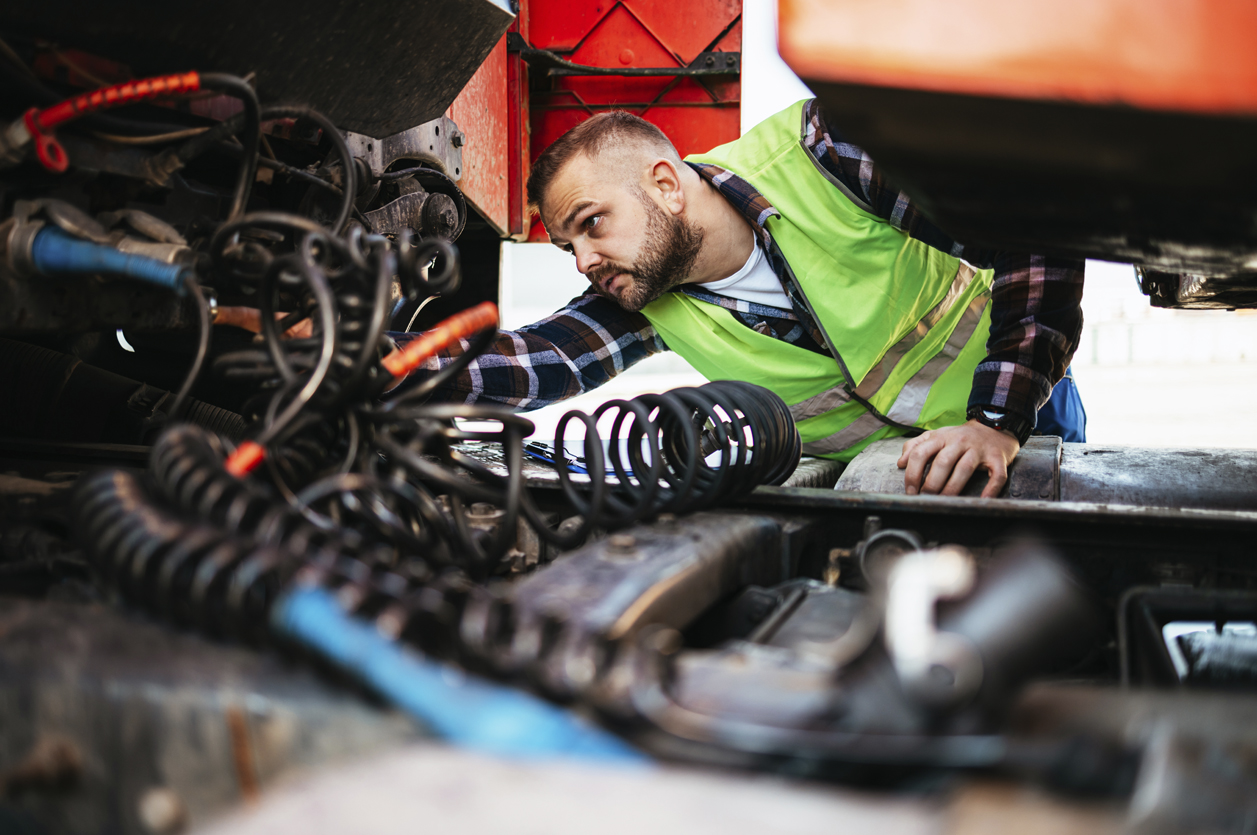 Truck Safety Inspector A safety inspector in a neon work vest inspects the connections and wiring under a semi truck.