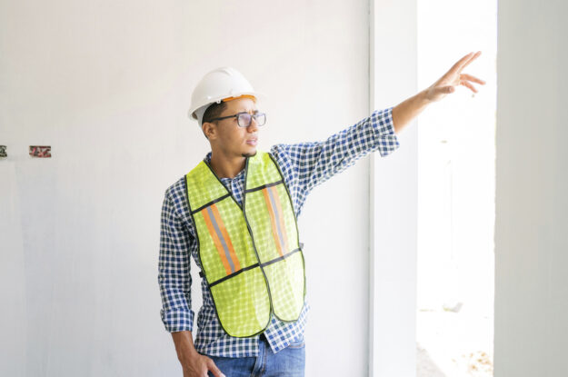 Ethnic male safety supervisor in neon vest and hard hat.