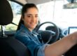 Female in driver's seat of car, turning to look at camera over her shoulder.