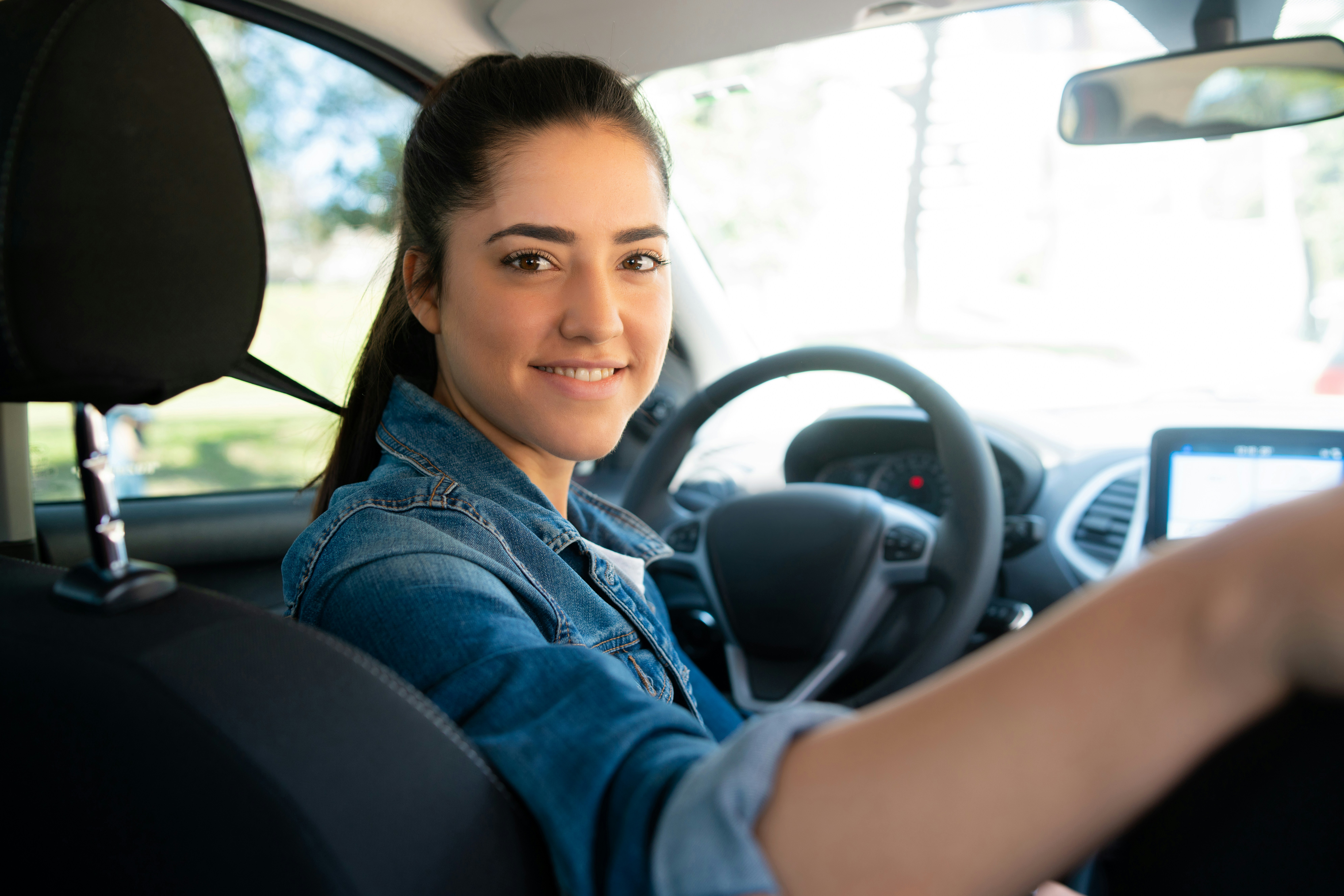 Female in driver's seat of car, turning to look at camera over her shoulder.