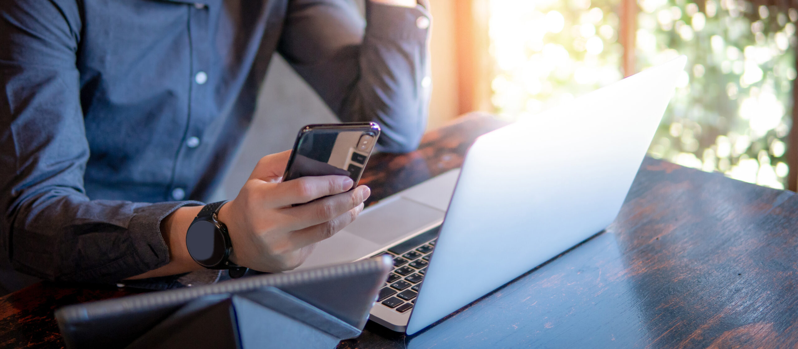 Male hand holding smartphone. Businessman using laptop computer and digital tablet while working in the cafe.