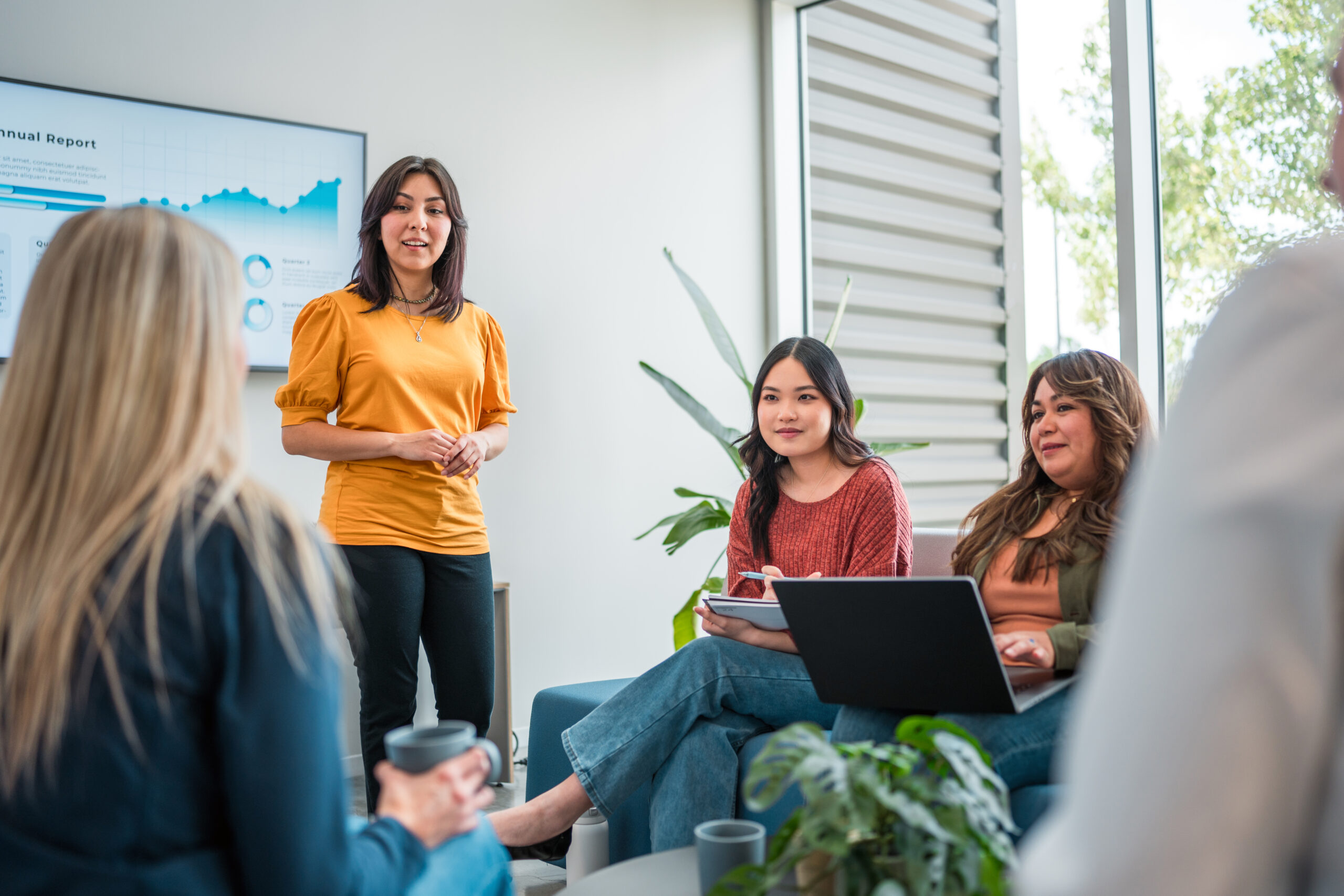 Professional Presentation by Hispanic Businesswoman A businesswoman confidently presents data, engaging with diverse colleagues during a team meeting in a well-lit office space.